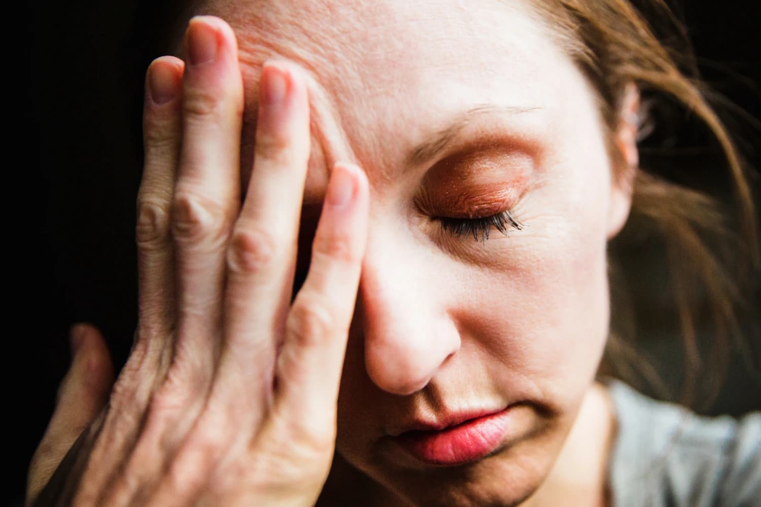Woman pressing her hand to her forehead with eyes closed from migraine pain